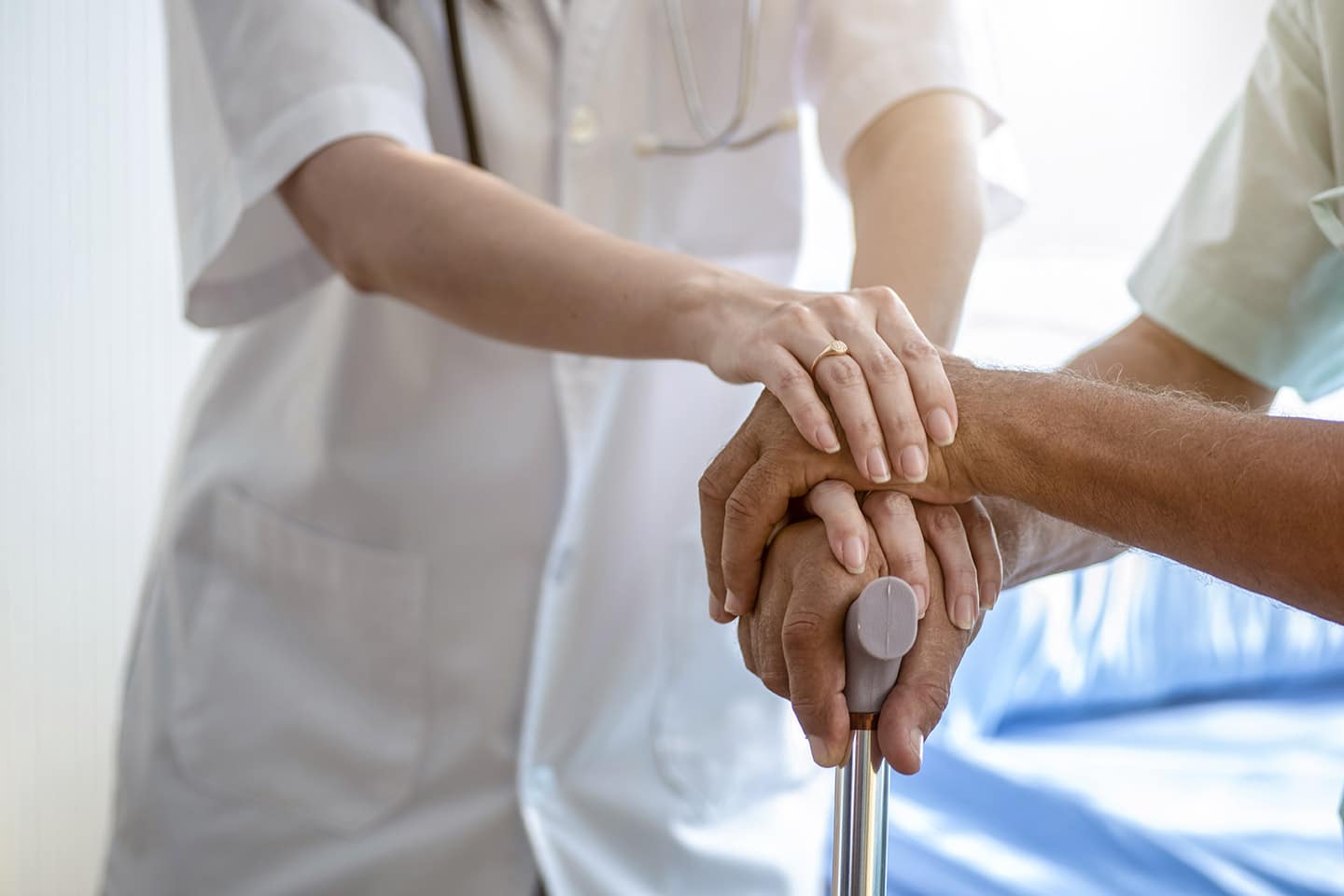 A nurse resting a hand over an older patient’s hands, folded on the top of a walking cane