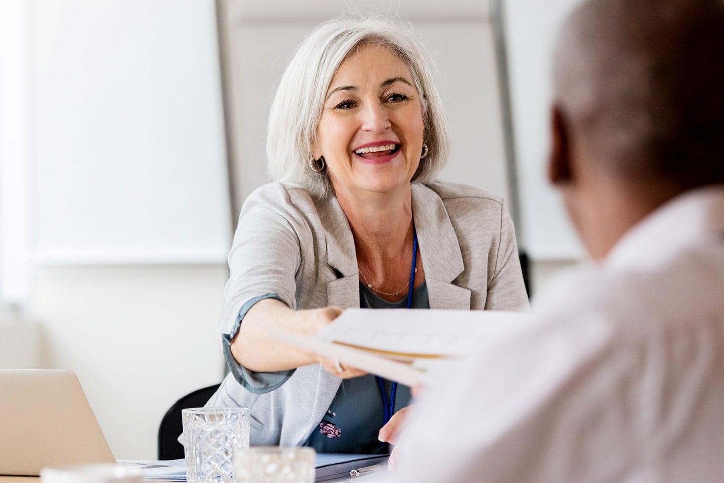 A Trustbridge adviser smiling as she hands a folder of documents across a desk to a client