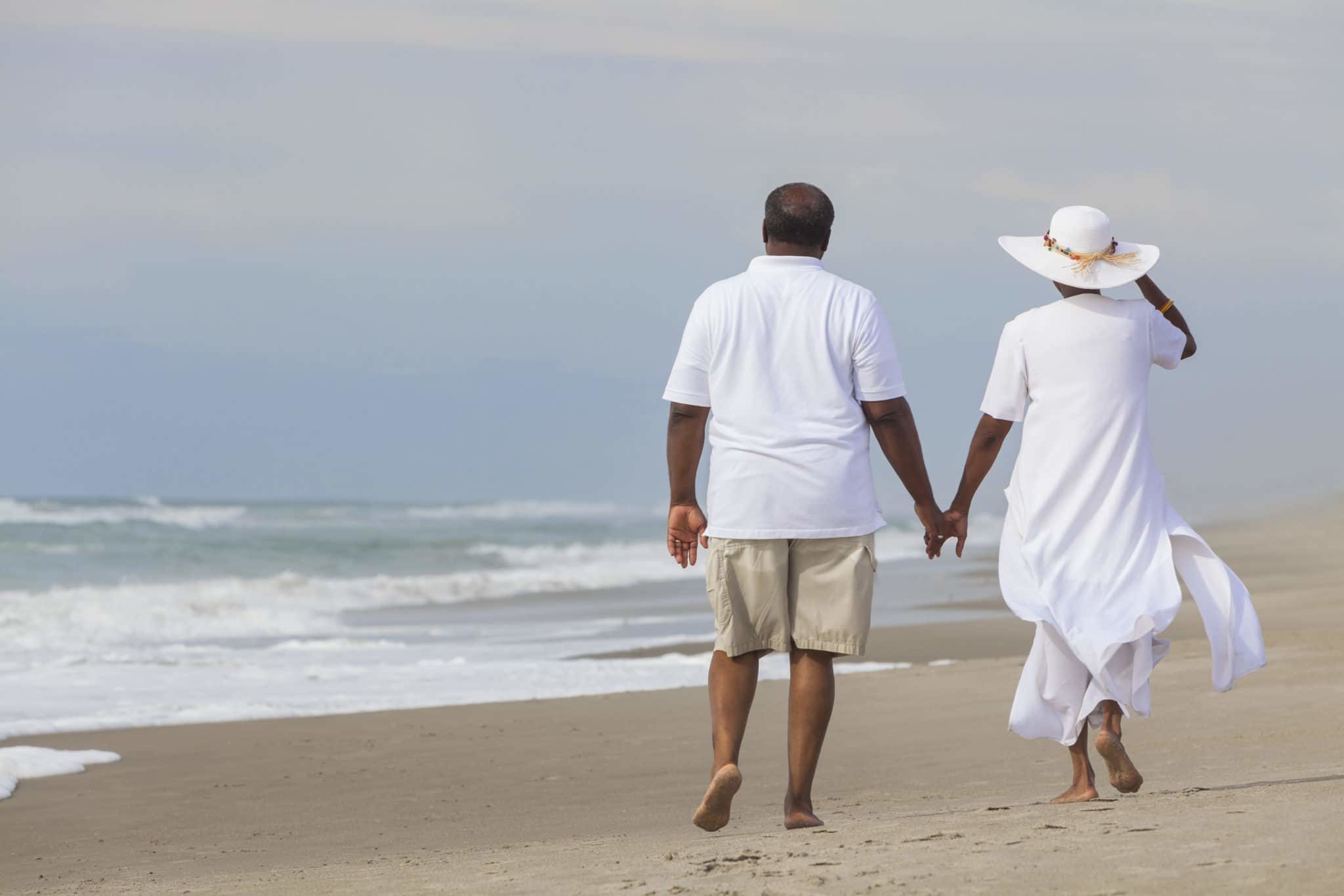 An older couple walking hand in hand along the shoreline