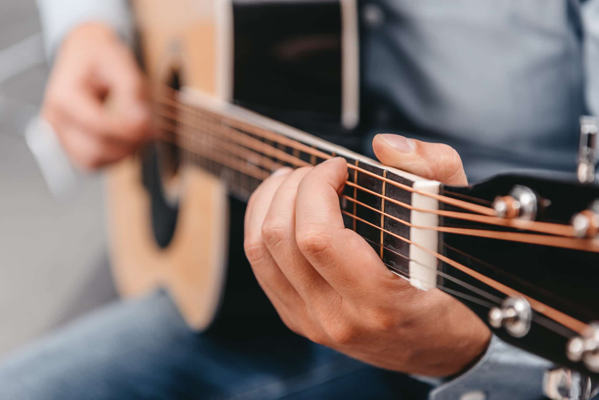 A man playing an acoustic guitar, one hand shaping a chord on the fretboard