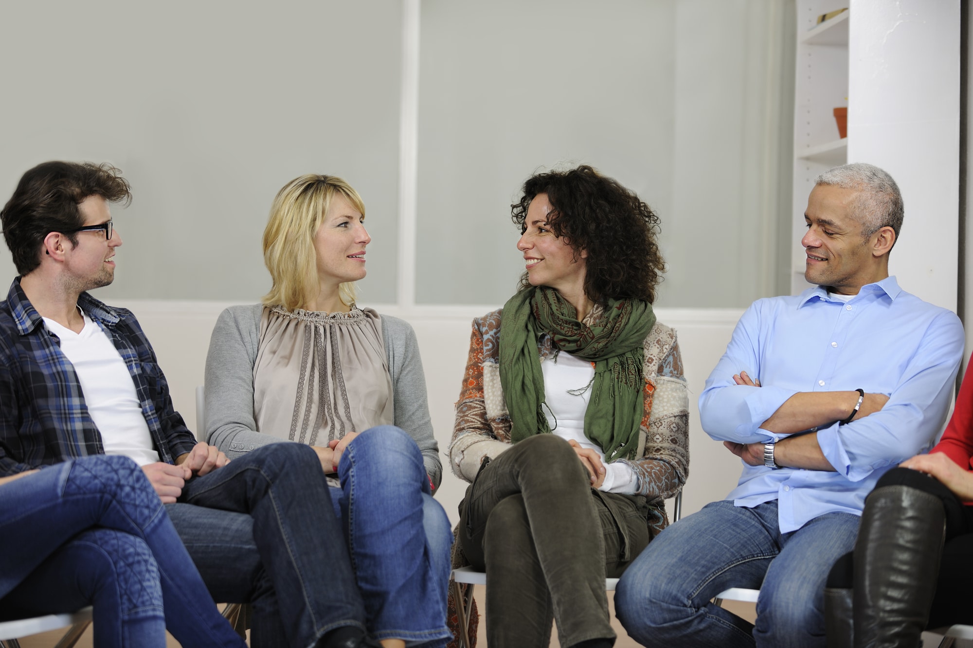 Four people sitting in a circle of chairs, talking together in a support group