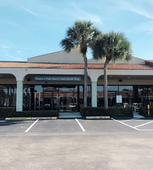 The Juno Beach resale shop storefront under two palm trees, its sign reading Hospice of Palm Beach County Resale Shop