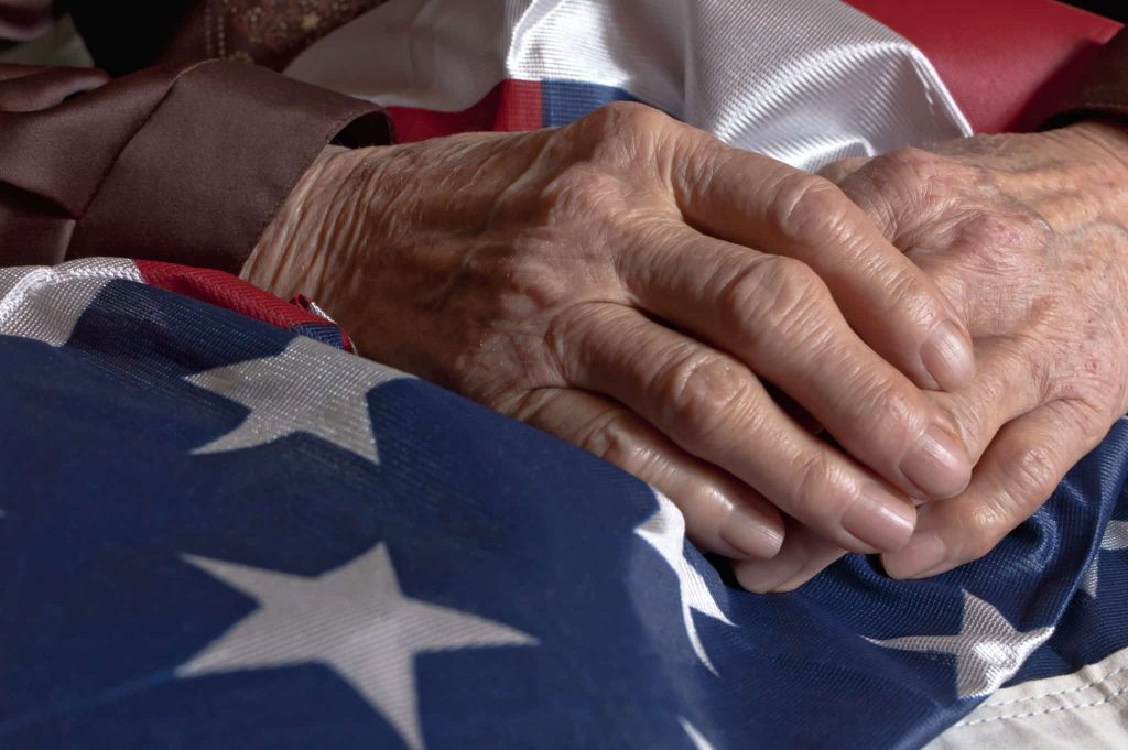 An older person’s hands resting on a folded United States flag