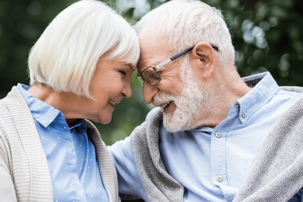An older couple resting their foreheads together, smiling, outdoors