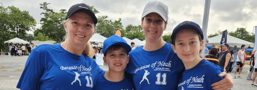 Four of Noah’s family and friends in matching blue Because of Noah number 11 shirts and caps at an outdoor event